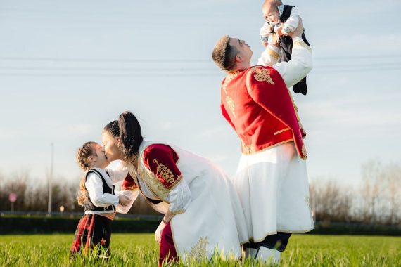 Joyful family in traditional attire playing in a sunny field, embracing cultural heritage.