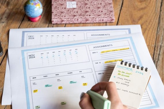 Person planning tasks with a calendar and notepad on a wooden table.